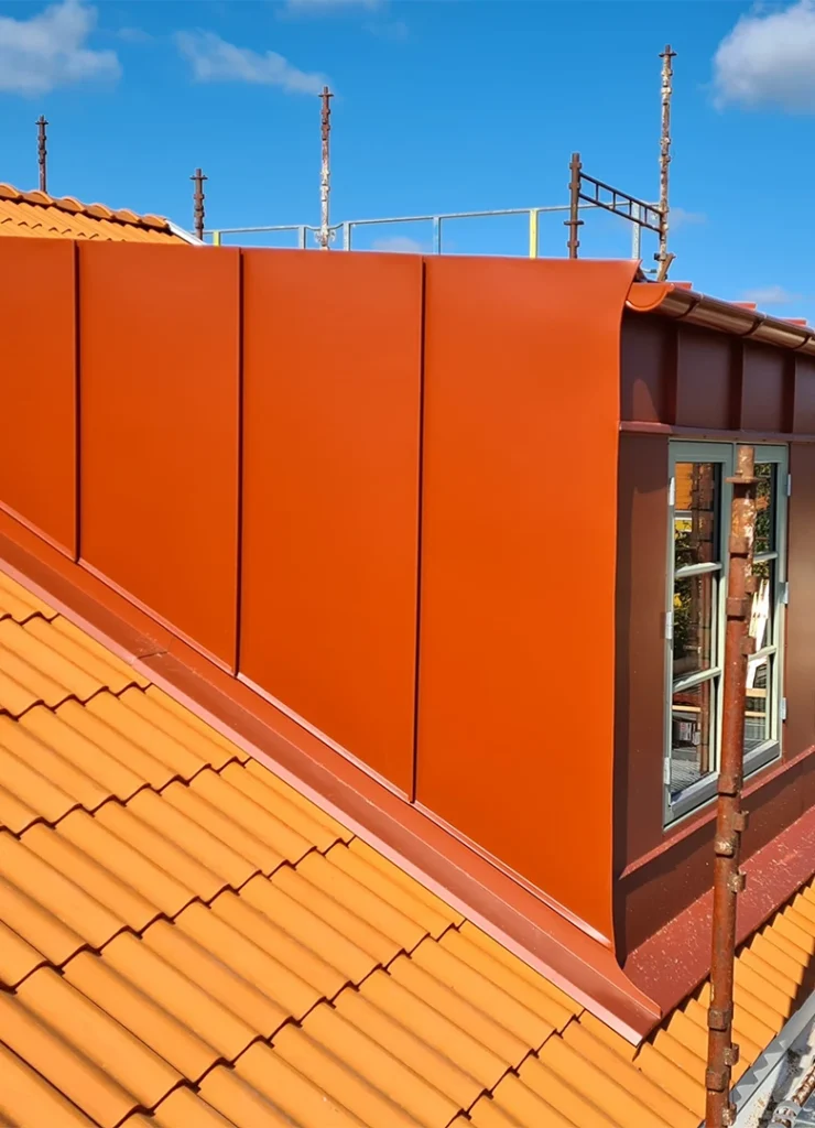 Röd plåtinklädd takkupa mot orange tegeltak