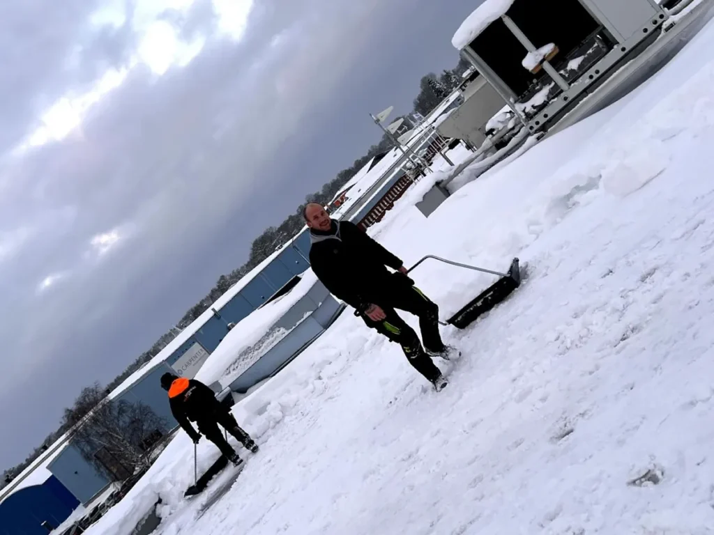 Plåtslagare skottar snö från ett lutande tak i Mönsterås